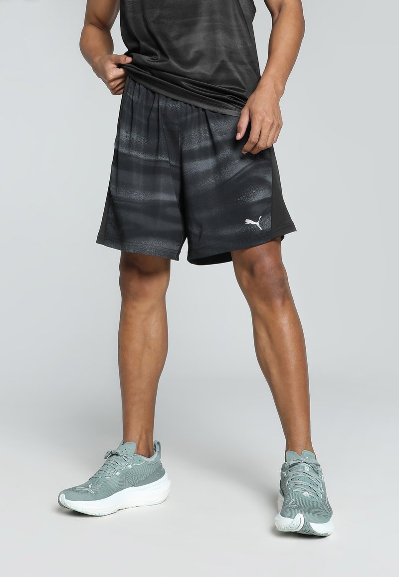 Svarta träningsshorts med en texturerad mönstring, elastisk midja och Puma-logga. Bärs tillsammans med ljus teal löparskor med vita sulor.