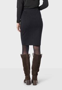 Černá tužková sukně s přiléhavým střihem, hladkou texturou a čistou siluetou, spárovaná s hnědými semišovými kozačkami ke kolenům s masivním podpatkem.