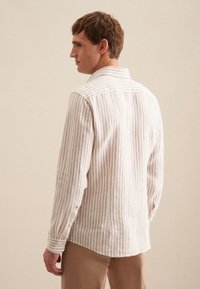 Camicia leggera in lino con righe verticali beige e bianche; presenta un colletto a punta e polsini con bottoni. Tessuto morbido, vestibilità rilassata.