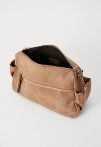 Sac en toile brun avec fermeture éclair, poche extérieure, accents en cuir et design minimaliste. Texture douce avec des détails cousus.