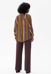 Striped long-sleeve shirt in green, brown, and cream with a collar; paired with wide-leg brown pants. Lightweight fabric with a loose fit.