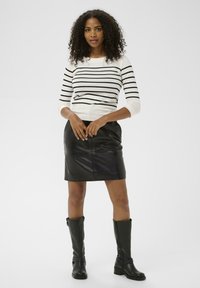 Pull rayé noir et blanc à manches trois-quarts, associé à une mini-jupe en cuir noire et des bottes noires montantes jusqu'au genou.