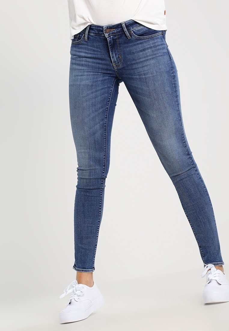Jeans ajustados de mezclilla azul oscuro, con un diseño clásico de cinco bolsillos, un ligero desgaste y una cintura de altura media, combinados con zapatillas blancas.