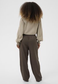 Kerge beež pluus puffed varrukatega ja volditud randmetega, millele on sobitatud laiad tumepruunid püksid; sile tekstuur ja lõdva istuvusega.