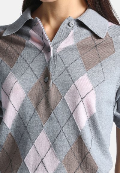 Femme portant un polo à manches courtes avec un motif argyle gris, rose et marron et deux boutons près du col.