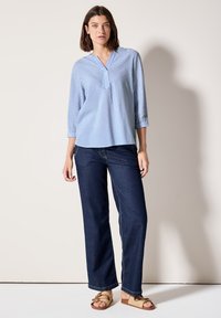 Blouse rayée bleue et blanche à manches trois-quarts, décolleté en V, associée à un jean droit bleu foncé et des sandales plates marron.
