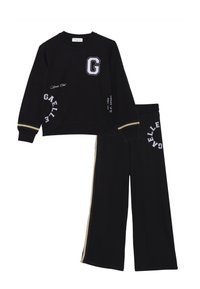 Il completo sportivo nero include una felpa con un logo "G" e testo bianco, e pantaloni larghi con strisce laterali dorate e dettagli ricamati.
