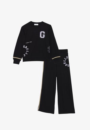 Il completo sportivo nero include una felpa con un logo "G" e testo bianco, e pantaloni larghi con strisce laterali dorate e dettagli ricamati.