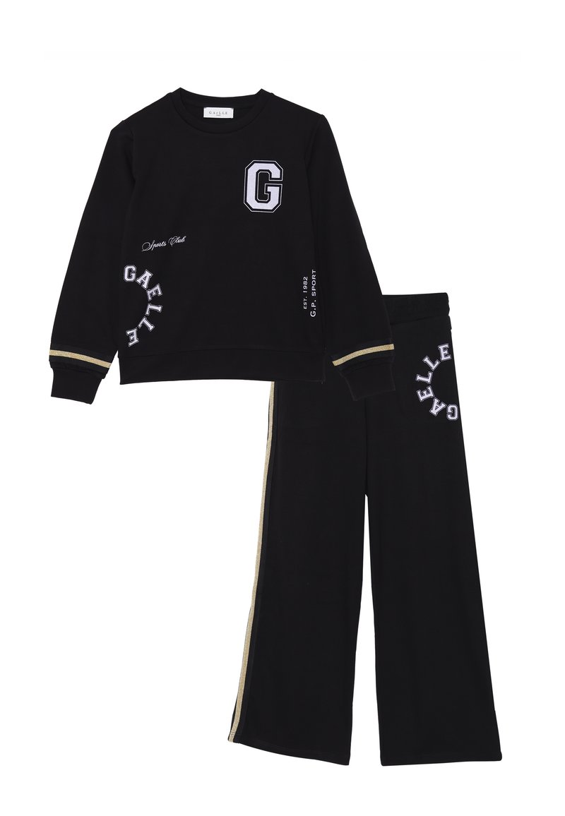 Il completo sportivo nero include una felpa con un logo "G" e testo bianco, e pantaloni larghi con strisce laterali dorate e dettagli ricamati.
