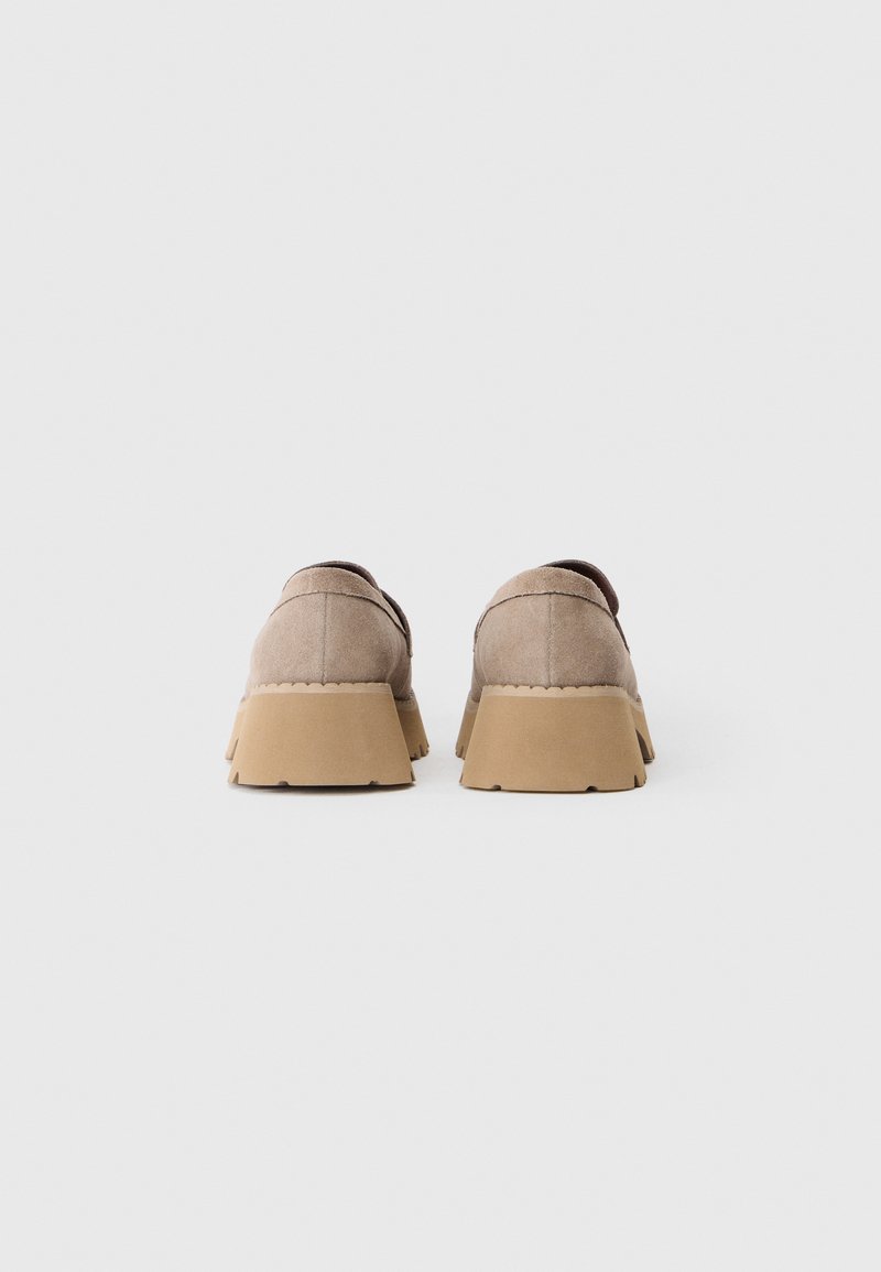 Beige Wildlederschuhe mit einem abgerundeten Design und dicken, gezackten, hellbraunen Gummisohlen. Die Rückseite hat einen flachen Schnitt und minimale Nähdetails.