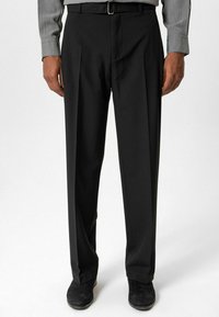 Zwarte pantalon met een getailleerde pasvorm, gladde stof, plooi aan de voorkant, zijzakken, gecombineerd met een grijs overhemd en zwarte schoenen.