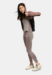 Träningskläder med en åtsittande, ljusgrå topp och matchande tights. En svart och rosa jacka är delvis nerdragna. Vita sneakers med gula detaljer.