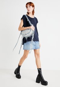 Marine t-skjorte, lys blå denim miniskjørt og svarte plattform ankelstøvler. En rund, frynset denimveske med lange stropper bæres.