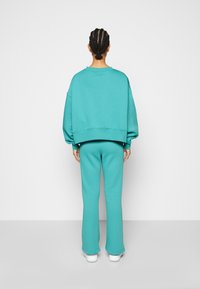 Turquoise oversized sweatshirt and matching flared sweatpants. Soft, smooth fabric with ribbed accents. White shoes complete the outfit.