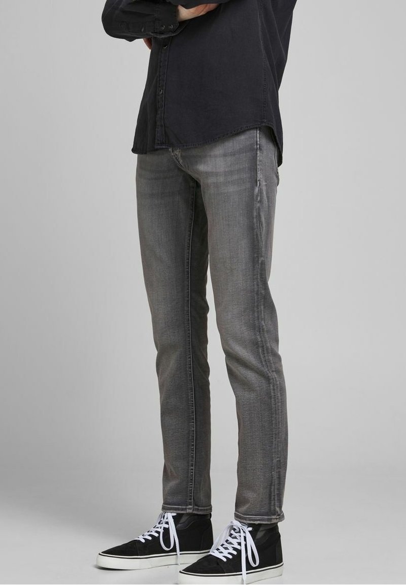Jeans ajustados grises con un lavado desgastado, que cuentan con bolsillos delanteros y traseros, combinados con zapatillas negras y cordones blancos.