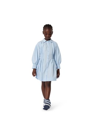 Hellblaues Baumwollkleid mit Puffärmeln, durchgehendem Knopfverschluss und geraffter Taille. Kombiniert mit marineblauen und weißen Turnschuhen.