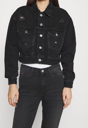 Woman wearing a black cropped denim jacket with silver buttons and distressed details, paired with high-waisted black jeans.