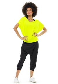 Fluorescent yellow oversized t-shirt paired with black harem-style pants, featuring elastic cuffs and a loose fit. White sneakers complete the outfit.