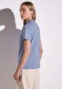 Světle modrý krátký rukáv top vyrobený z měkké látky, s kulatým výstřihem a rovného střihu. Model je kombinován s kalhotami v neutrálních barvách.