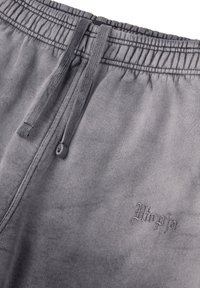 Pantalones de chándal grises con cintura elástica, cordón y logo bordado "Utopia". La tela tiene una textura suave y lisa.