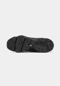 Black sneaker sole with textured rubber, featuring circular and wave patterns, and visible brand logo. Bold tread design for grip.