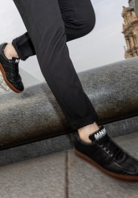 Svarta lädersneakers med en texturerad yta, gummisulor och kontrasterande vit märkning på tungan. Bärs med mörka byxor.