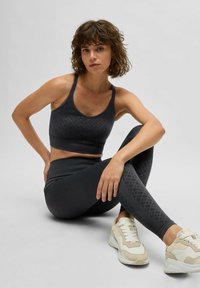 Musta urheilutoppi ja legginsit, joissa on tekstuurikuvio, yhdistettyinä vaaleisiin urheilukenkiin, joissa on verkkokudosta ja mokkaa.