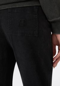 Schwarze Denim-Jeans mit einer Gesäßtasche mit geprägt Champion-Logo, subtiler Textur und geradem Beinschnitt.