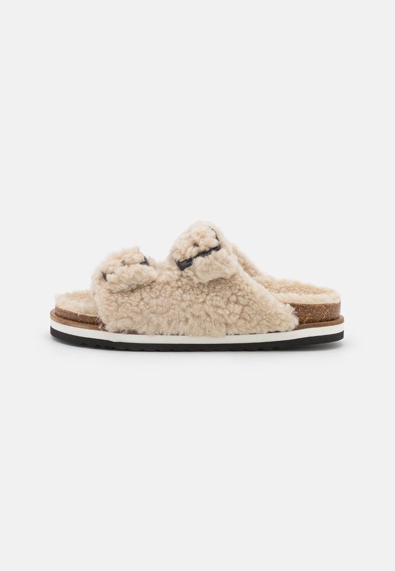 Flauschige, beige Riemensandalen mit zwei Oberriemen und schwarzen Akzenten. Verfügt über ein Korkfußbett und eine weiße Zwischensohle mit schwarzem Außensohl.