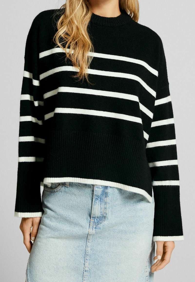 Black and white striped knit sweater featuring a ribbed hem, round neckline, and relaxed fit, paired with a light denim skirt.