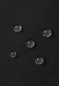 Fünf Wassertropfen liegen auf strukturiertem schwarzem Stoff und zeigen die Oberflächenspannung sowie die Details des Stoffes darunter.