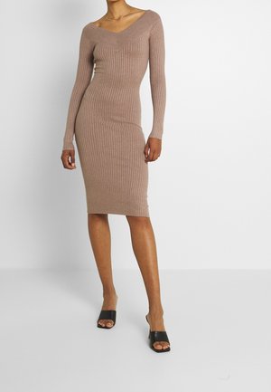 Robe ribbed à manches longues, ajustée, en taupe doux avec un décolleté en V. La robe présente une coupe slim et arrive au genou, associée à des talons ouverts noirs.