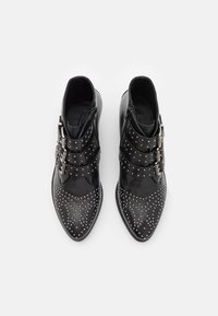 Botines negros con punta afilada, detalles de tachuelas y tres hebillas decorativas. Fabricados en cuero con una textura suave y cremalleras laterales.