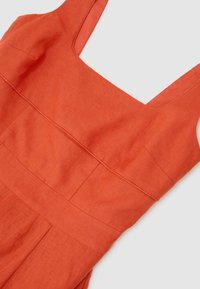Robe en lin orange sans manches avec un col carré et une taille cintrée, étalée à plat sur un fond gris clair.