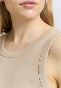 Débardeur côtelé beige avec un col rond et de larges bretelles, confectionné en tissu doux avec une texture lisse et un minimum de détails de couture.