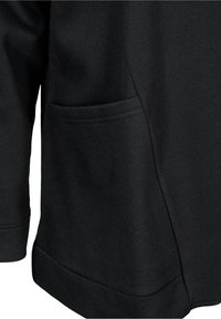 Vêtement noir à manches longues avec une poche frontale latérale et des coutures visibles le long de l'ourlet et des bords de la poche.