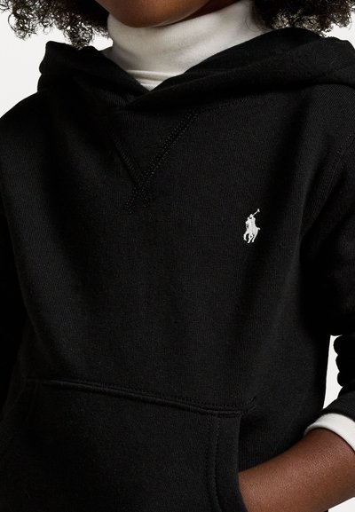Svart hoodie med en framficka i kängurustil och en vit broderad logotyp. Har en huva med dragsko och ribbade ärmslut tillsammans med en lager-på-lager vit turtleneck.