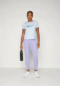 Lyseblå t-skjorte med en turkise Nike-logo, kombinert med lavendelfargede leggings. Figuren holder en svart vannflaske og har på seg hvite joggesko.