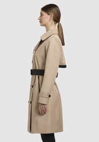 Beige trench coat with a belted waist, large collar, and button details. Features a straight cut and smooth texture.