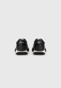Black athletic shoes with a textured leather upper, white accents, and a sturdy black sole. Logo displayed on the heel.