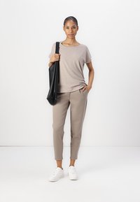 Beige t-skjorte med korte ermer, kombinert med lysebrune tapered bukser. En svart skulderveske og hvite joggesko fullfører antrekket.