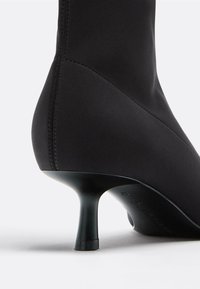 Černý vysoký podpatek boty vyrobené z hladké látky, s špičatou špičkou, úzkým podpatkem a bezproblémovou konstrukcí s viditelnými švy.