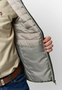 Zelená bunda so zipsom vpredu, so prešívanou vnútornou podšívkou svetlosivej farby a vnútornou vreckom. Exteriér je hladký.