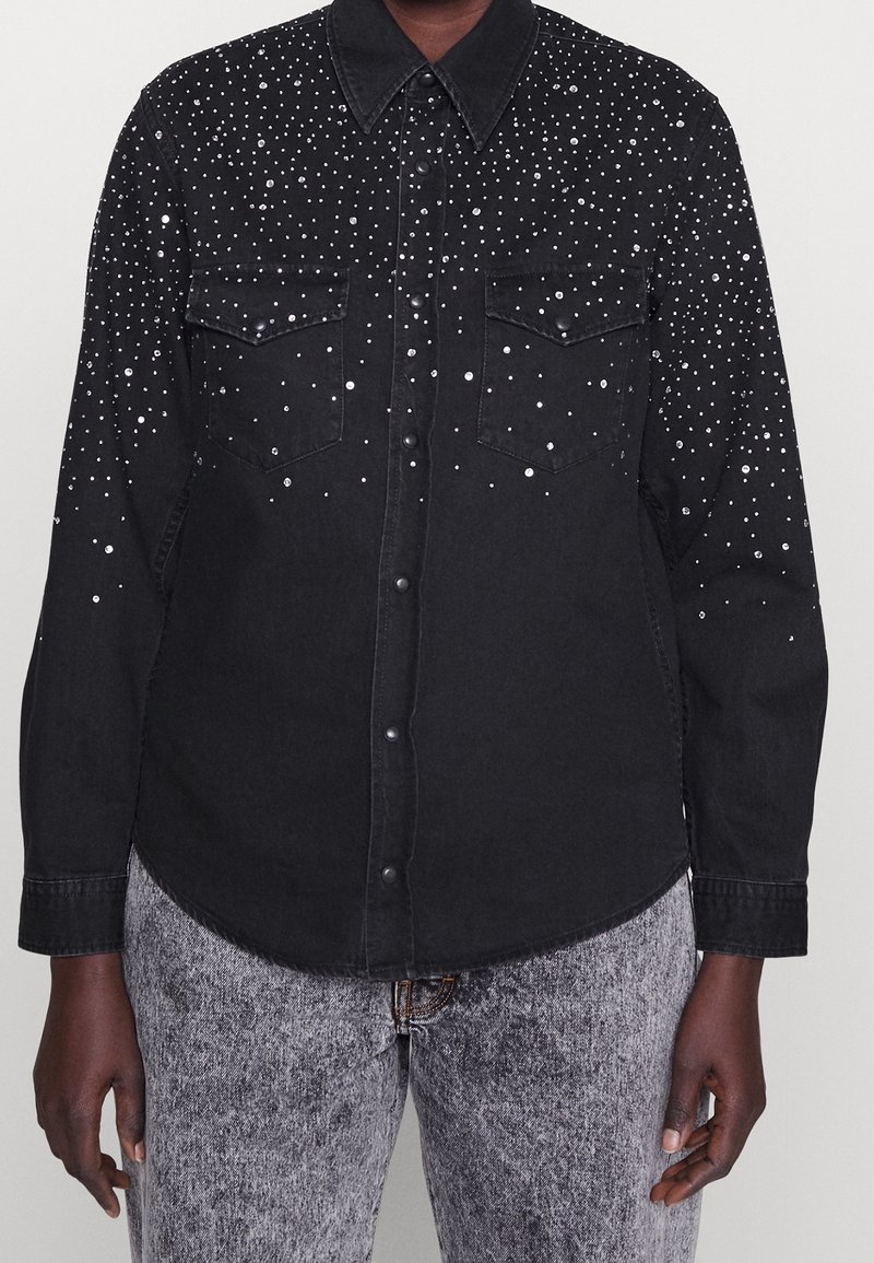 Black denim shirt with silver decorative studs, featuring two front pockets, a classic collar, and button closures. Textured fabric with a subtle sheen.