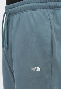 Κοντινό σε μπλε φλις παντελόνι με ρυθμιζόμενο κορδόνι, ελαστική μέση και λευκό λογότυπο The North Face πάνω από την πλαϊνή τσέπη.