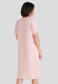 Vestido corto rosa de manga corta con cuello redondo, largo a la rodilla y tejido suave. Textura lisa sin patrones ni acentos visibles.