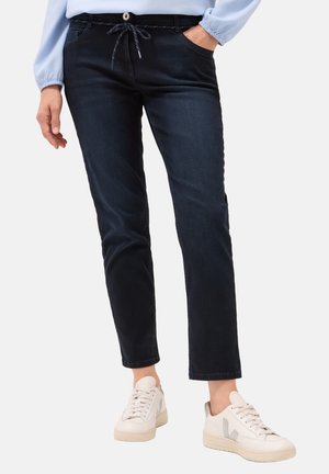 Pantalons en denim bleu foncé avec une taille élastique à cordon, des poches latérales et une coupe droite, associés à des baskets blanches.