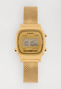 Relógio digital Casio dourado com bracelete de malha mostrando a hora 10:10 e rótulos para alarme, temporizador, modo, iniciar-parar e resistência à água.