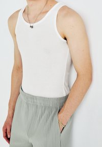 Top sin mangas blanco con canalé y tirantes anchos, combinado con pantalones suaves de color gris claro, con pliegues verticales y cintura elástica.