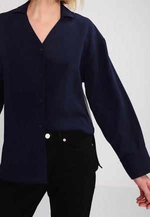 Navy blue long-sleeve shirt in smooth fabric with a V-neckline, button front, and relaxed fit. Paired with fitted black pants.